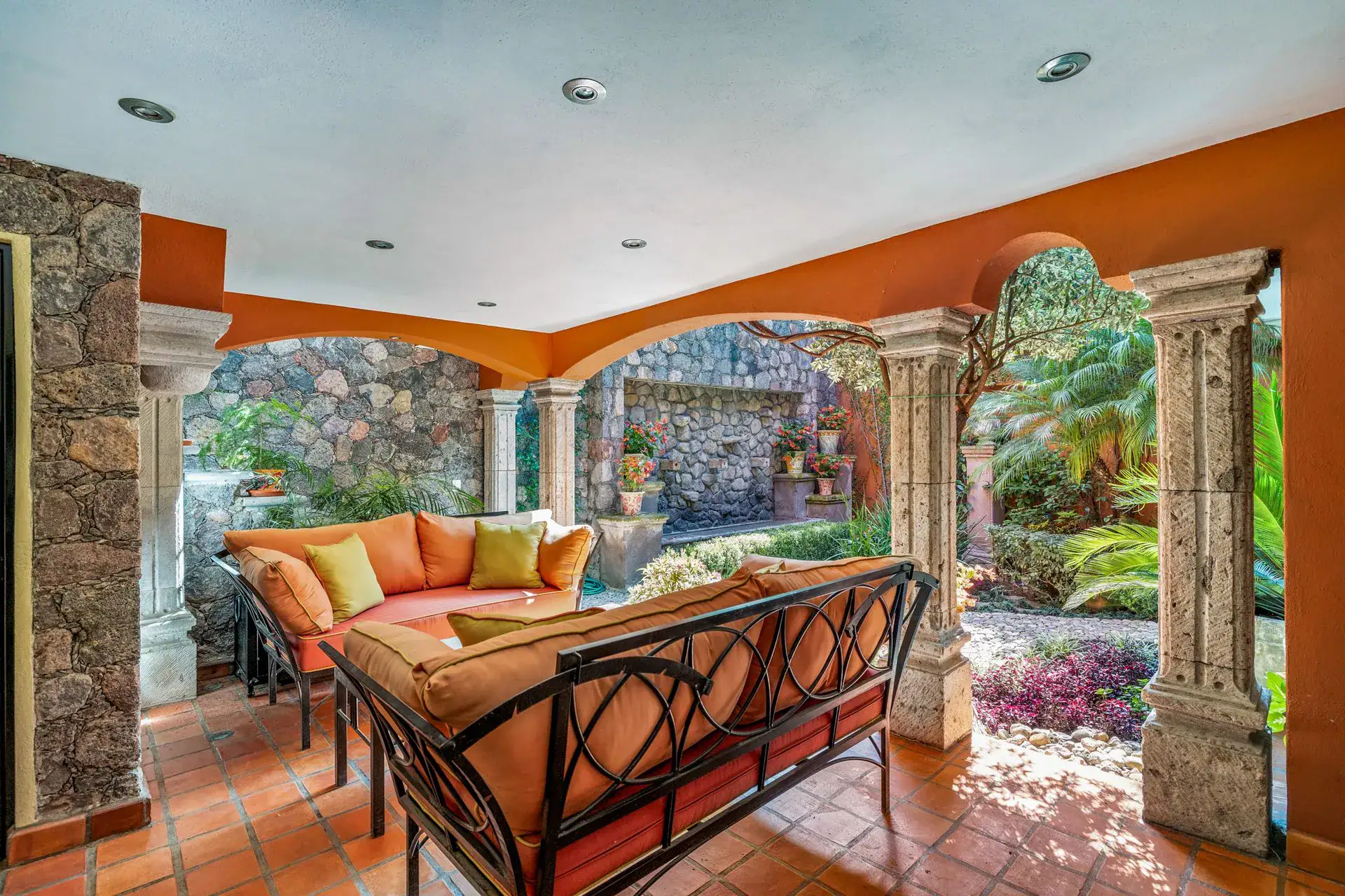 Casa Flora, covered loggia with an orange sofa and stone columns overlooking the garden, San Miguel de Allende