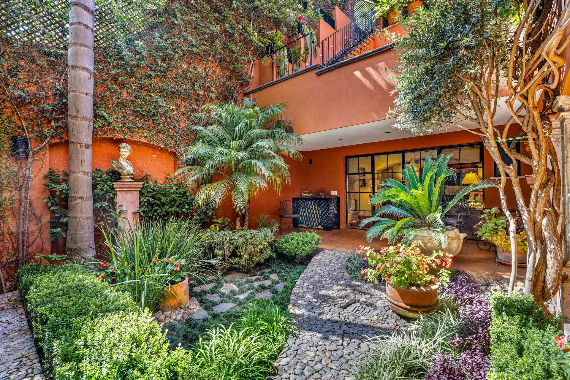 Casa Flora, garden with palms, clipped hedges and a bust under an orange wall, San Miguel de Allende