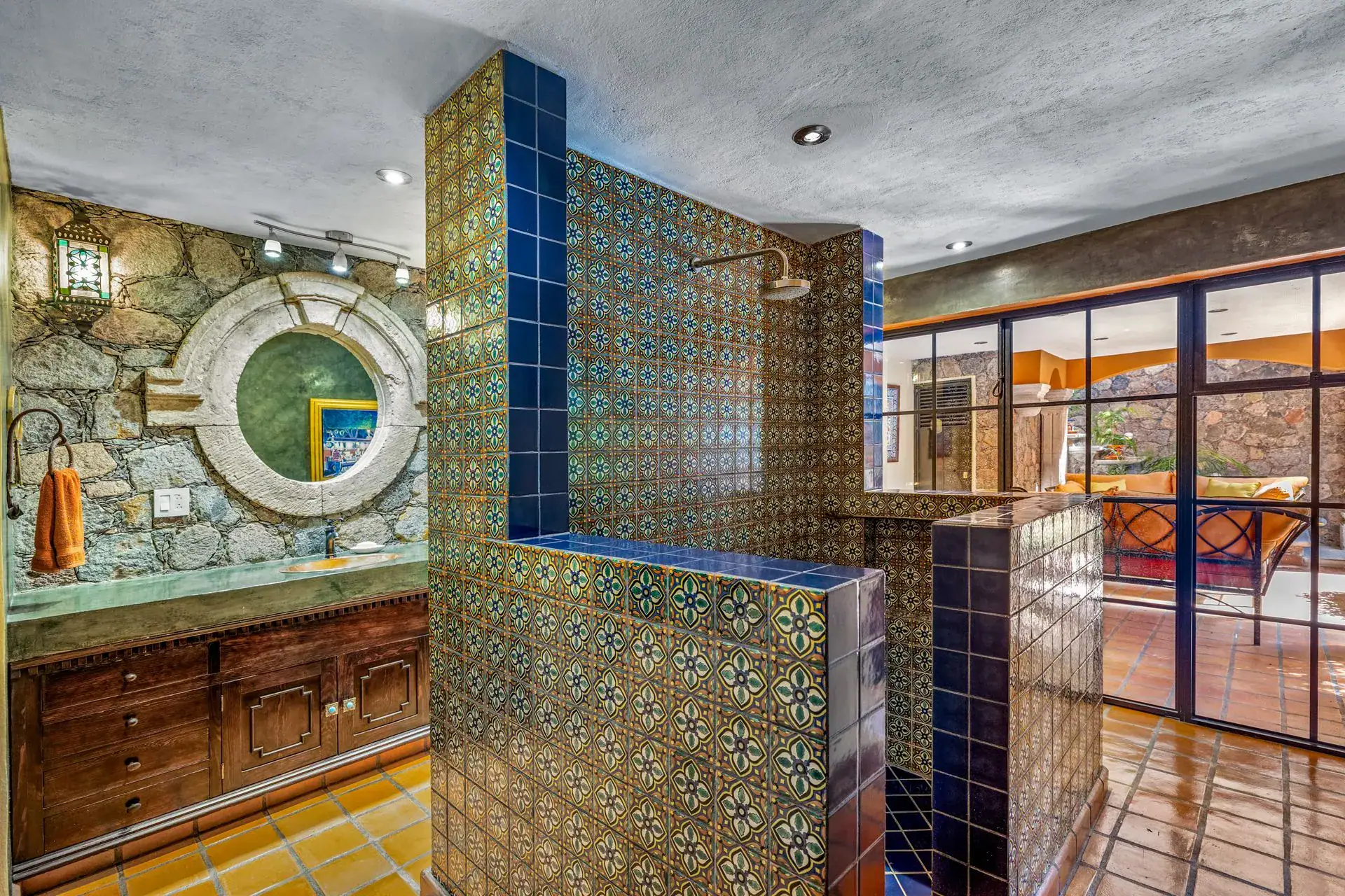Casa Flora, bathroom with a blue tile shower, a stone wall with a round window and a wood vanity, San Miguel de Allende