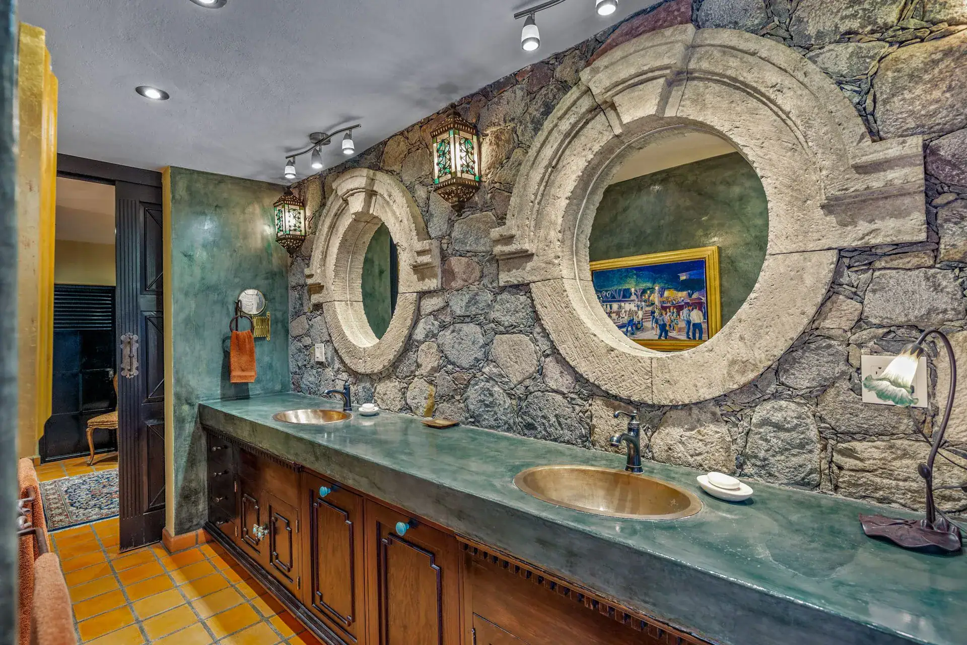 Casa Flora, bathroom with a long green counter, brass sinks and round stone-framed mirrors on a stone wall, San Miguel de Allende