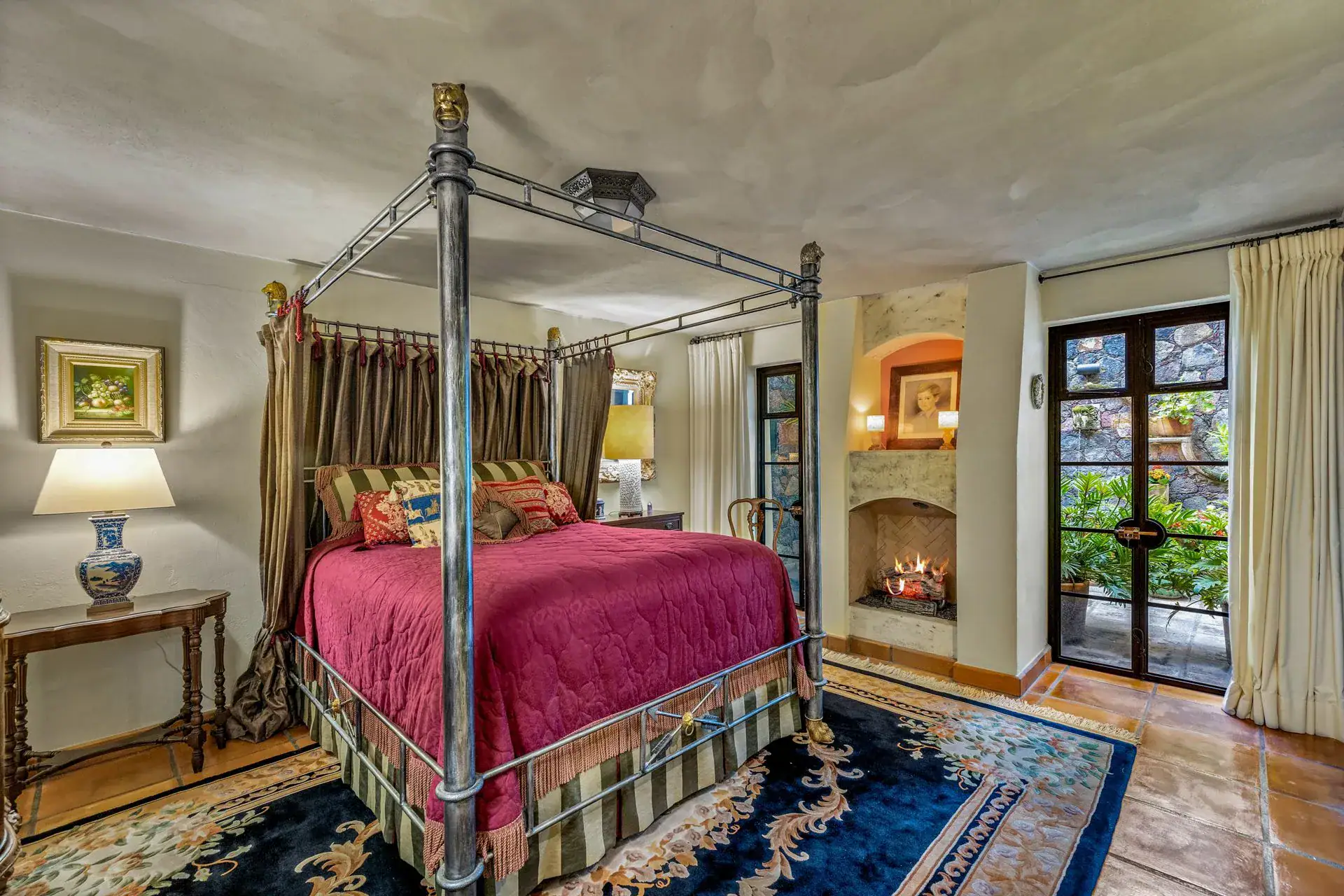 Casa Flora, bedroom with a canopy iron bed, a red quilt and a fireplace niche, San Miguel de Allende