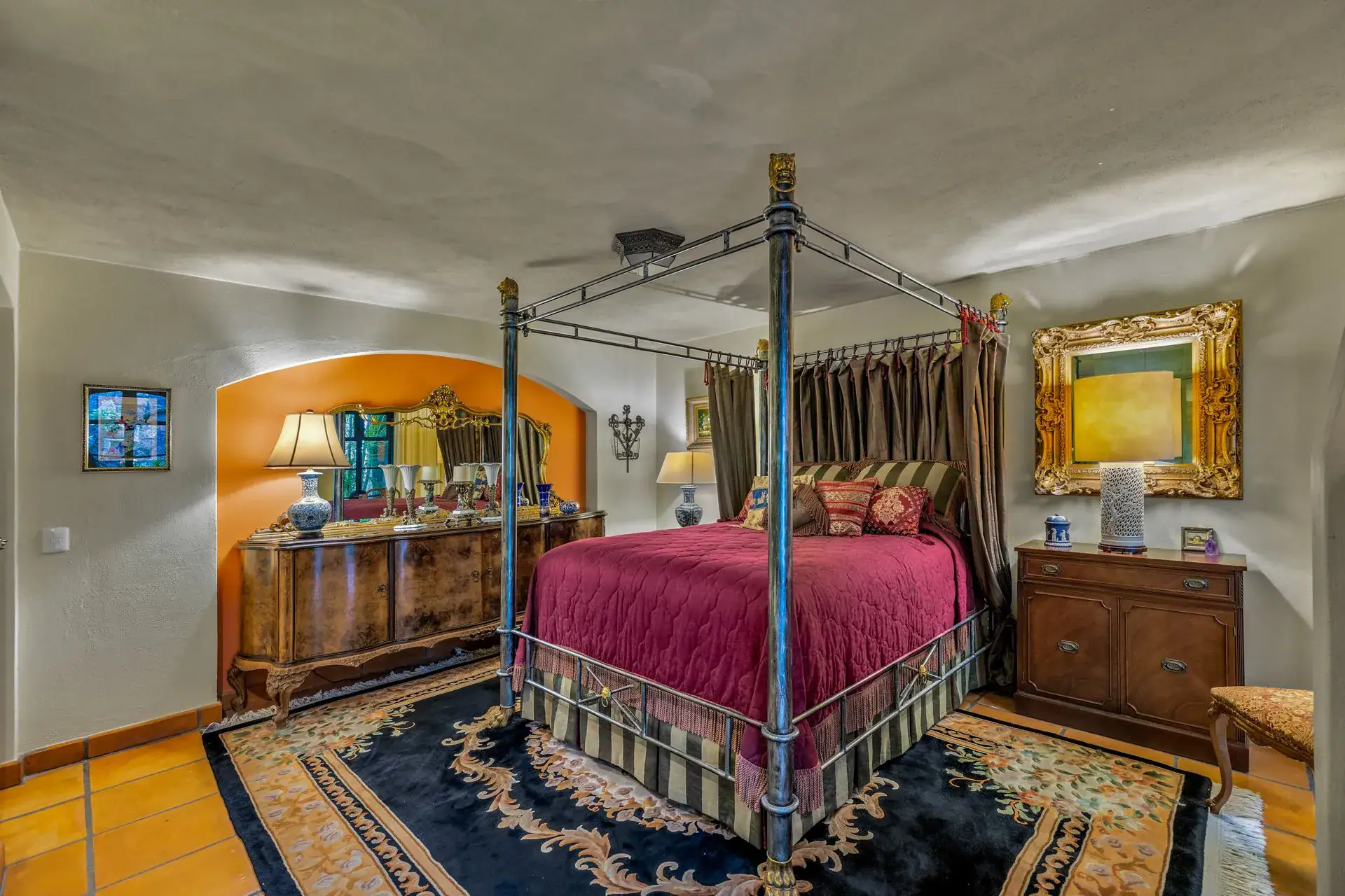 Casa Flora, bedroom with an iron canopy bed, a dresser, a gold mirror and an arched niche, San Miguel de Allende