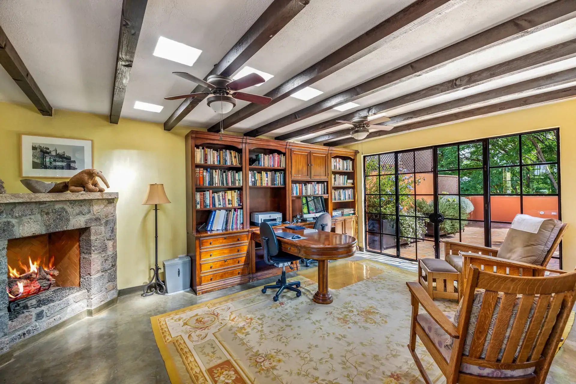 Casa Flora, study with a stone fireplace, bookshelves, a round desk and armchairs under a beamed ceiling, San Miguel de Allende