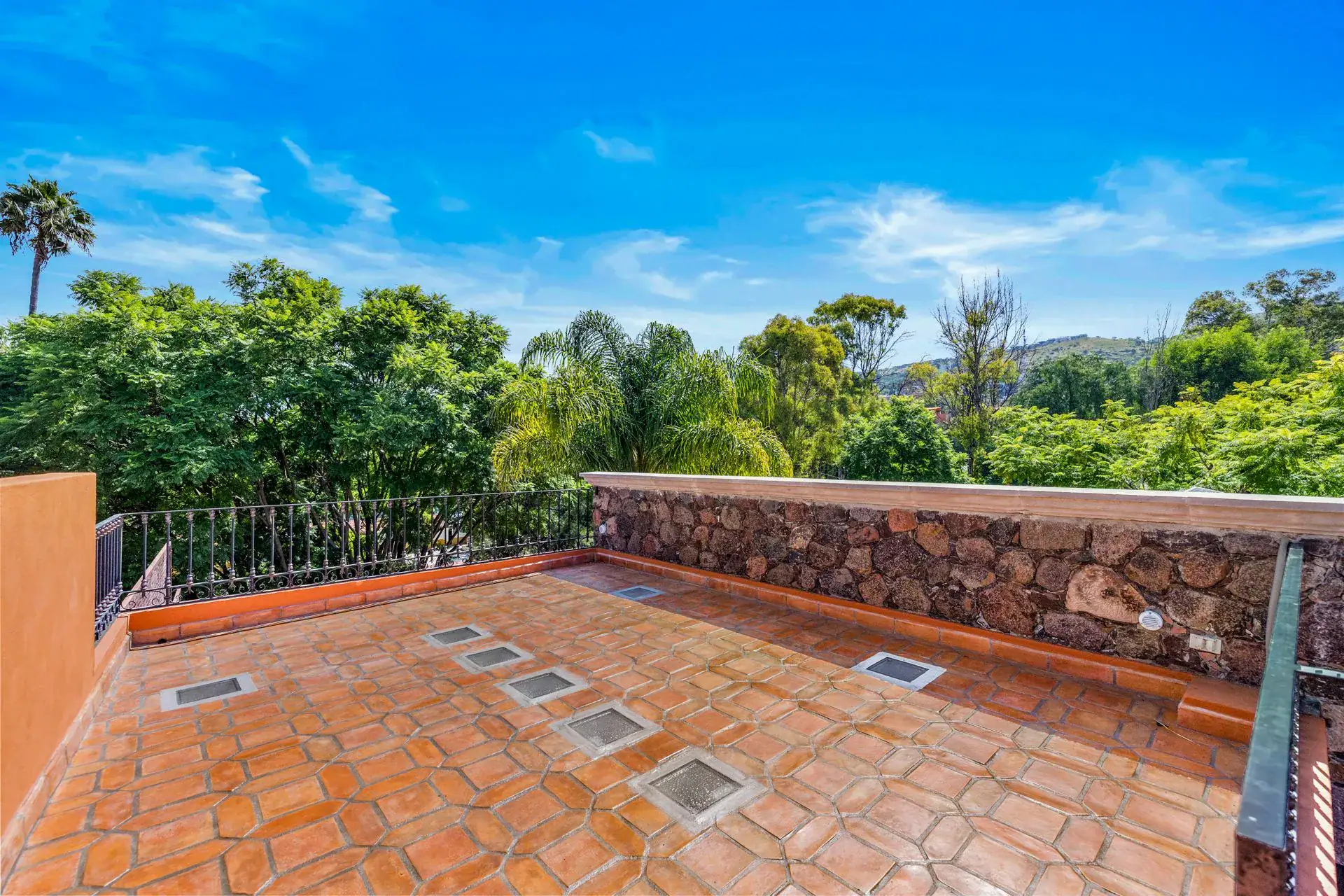 Casa Flora, roof terrace with a stone parapet, skylight panels and green hills beyond, San Miguel de Allende