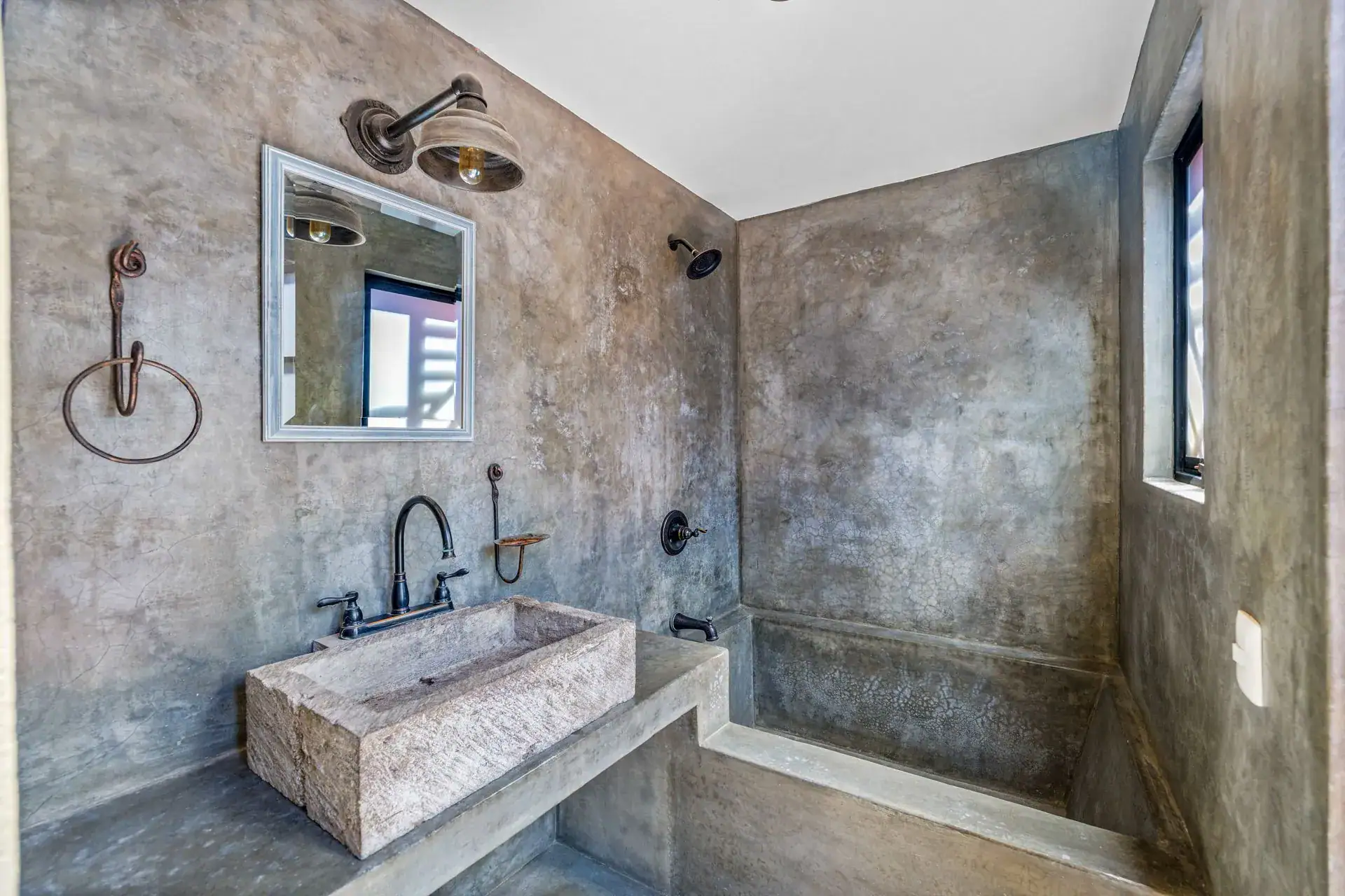Casa Flora, bathroom with a concrete wall, a stone trough sink and iron towel hooks, San Miguel de Allende