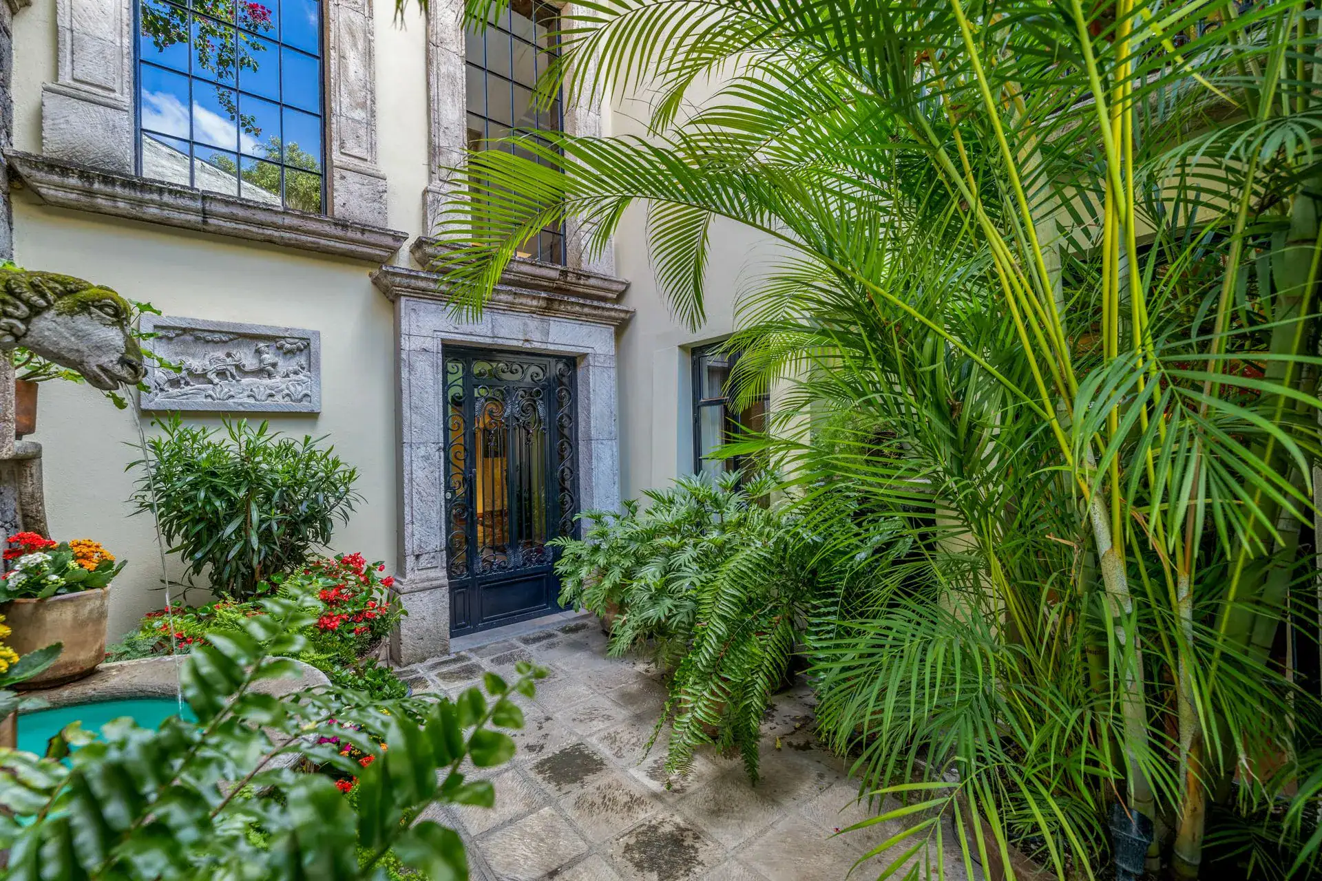 Casa Flora, stone-framed doorway to a courtyard with palms, flowers and a small fountain, San Miguel de Allende