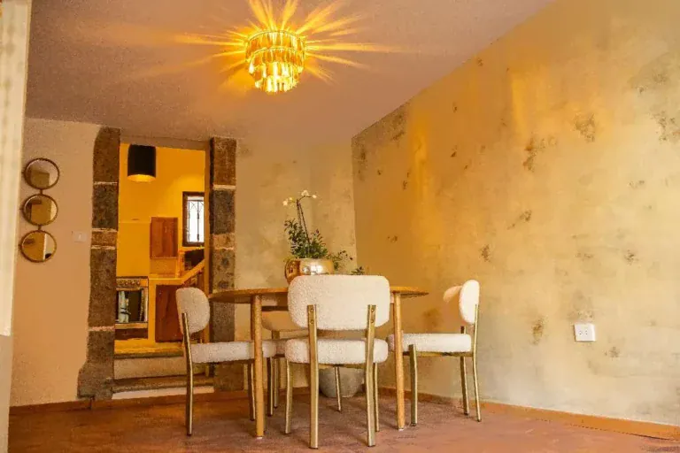 Casa Garza, dining table with white upholstered chairs beside a stone-framed doorway and a gold wall, San Miguel de Allende