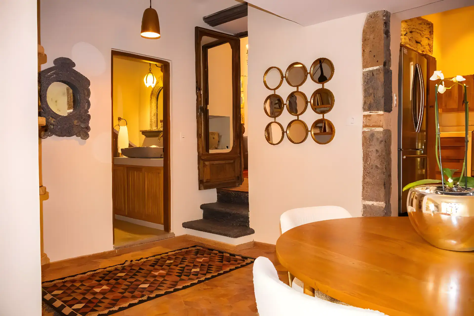 Casa Garza, hallway with a wood table, a bathroom with a stone sink beyond and a cluster of round mirrors, San Miguel de Allende