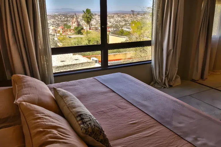 Casa Garza, bed with a view through a large window over the rooftops and the Parroquia, San Miguel de Allende