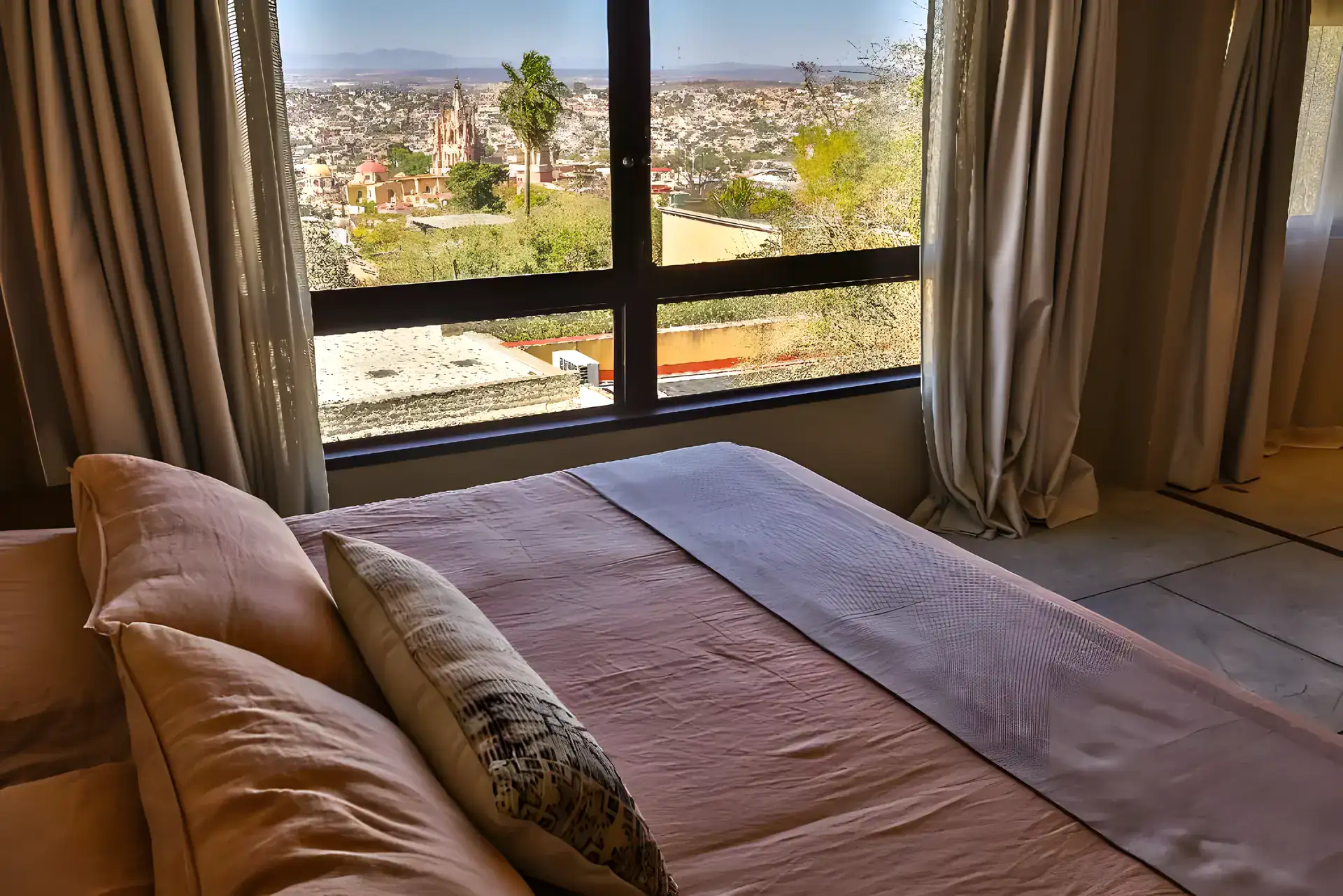 Casa Garza, bed with a view through a large window over the rooftops and the Parroquia, San Miguel de Allende