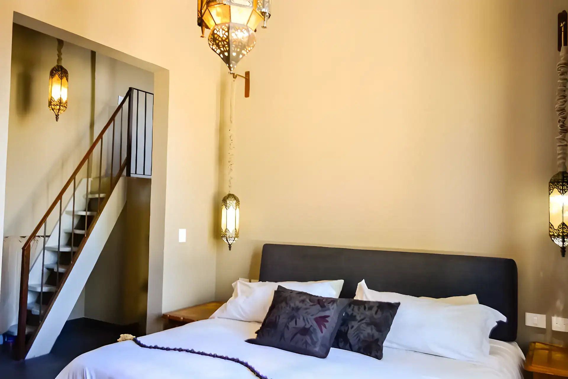Casa Garza, bedroom with a gray headboard, black and white pillows, tin lanterns and a metal staircase, San Miguel de Allende