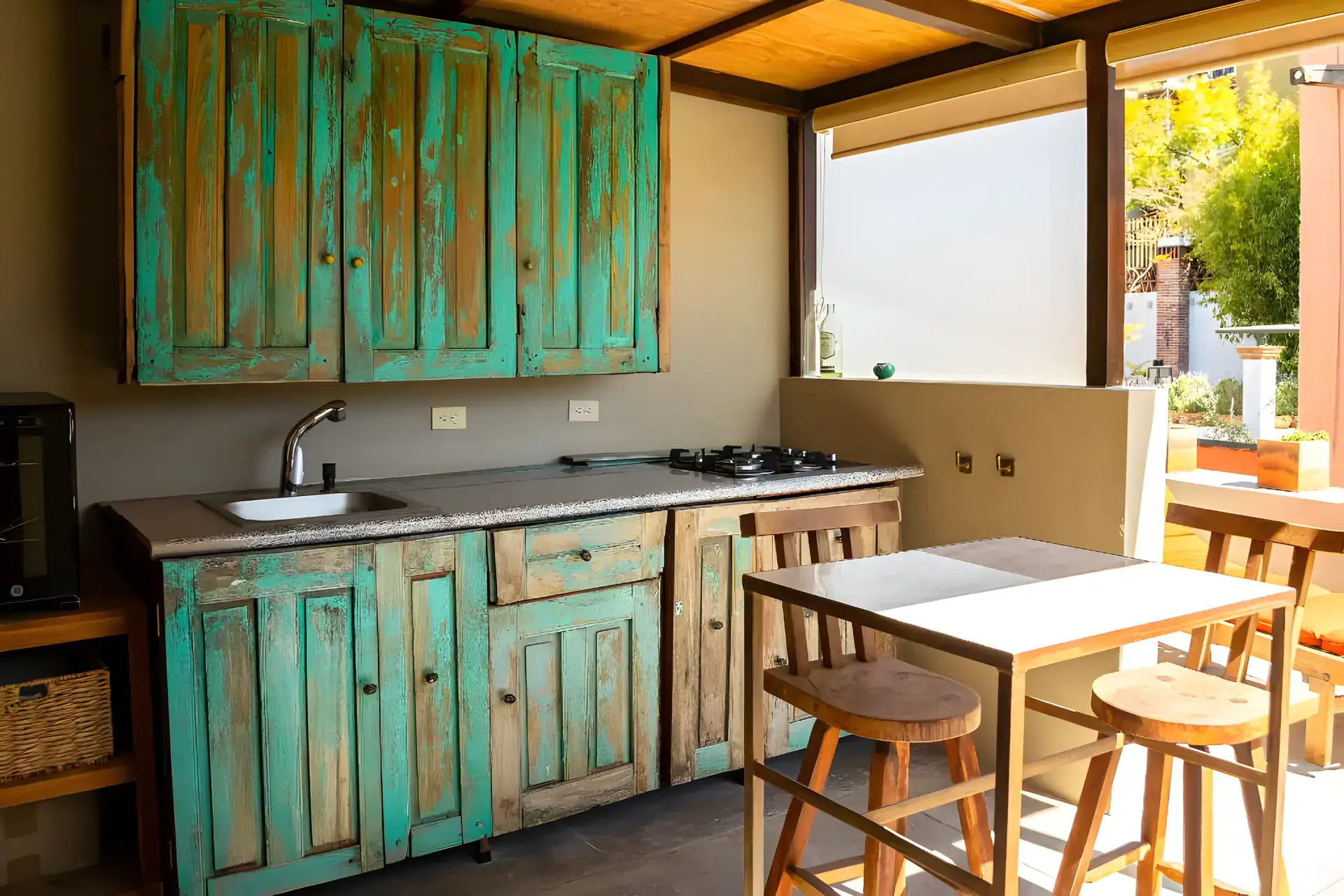 Casa Garza, outdoor kitchen with turquoise distressed wood cabinets, a sink, a cooktop and a table with stools, San Miguel de Allende