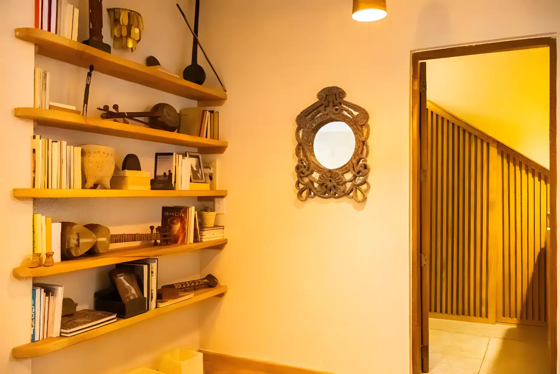 Casa Garza, bookshelf with books and instruments beside a staircase and a framed mirror, San Miguel de Allende