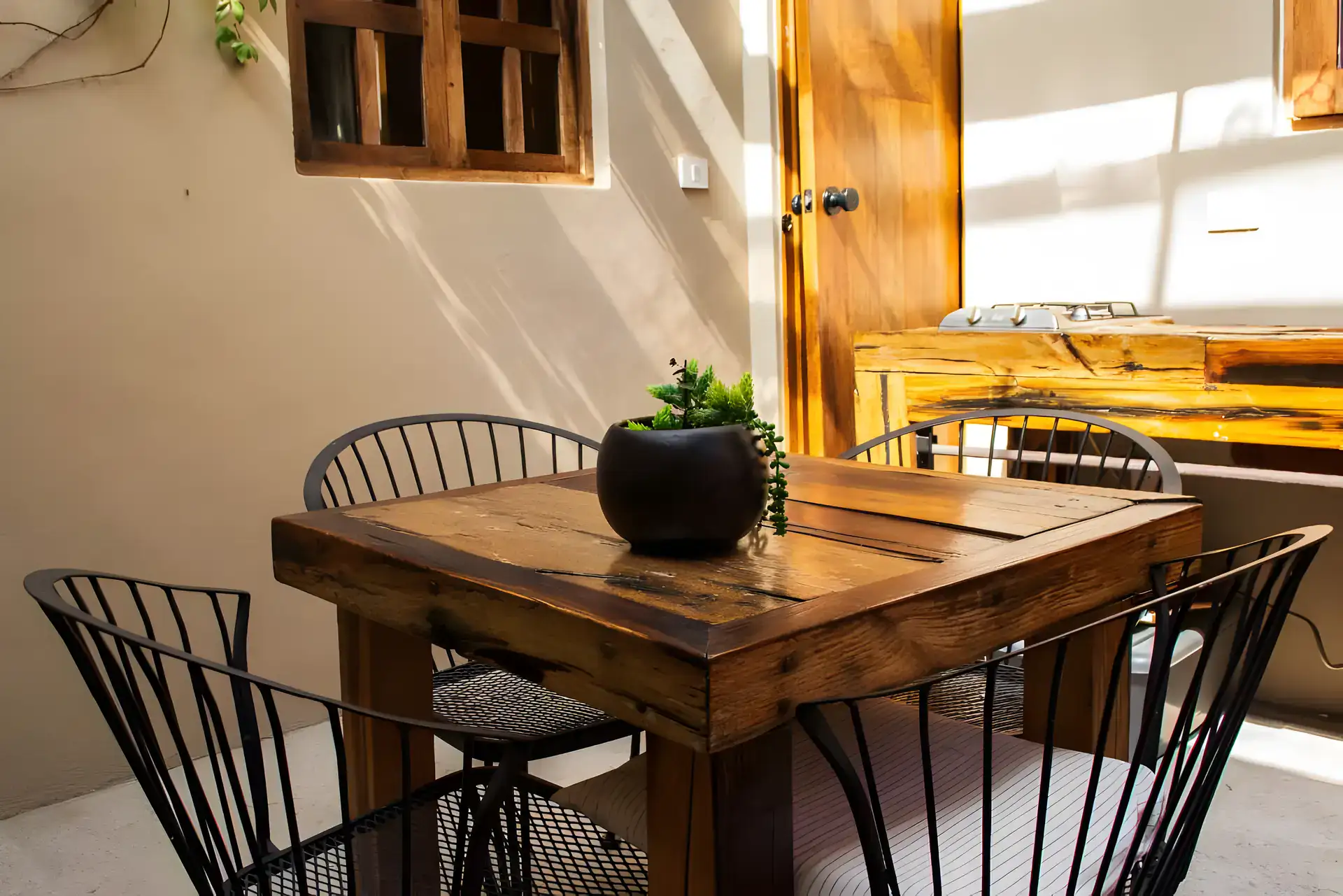 Casa Garza, courtyard dining table with metal chairs and a plant beside a wooden door, San Miguel de Allende