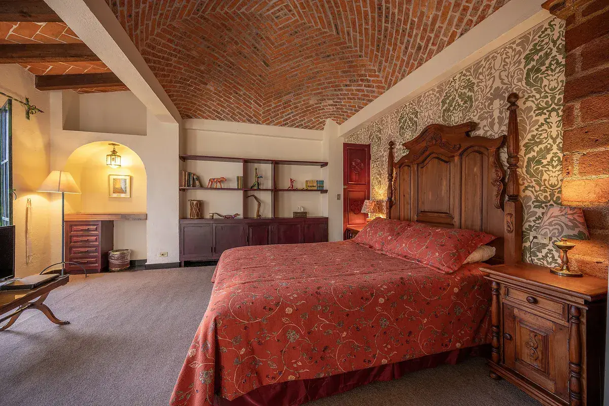 Casa Gracia, bedroom with a carved wood bed, a red bedspread and a brick vaulted ceiling, San Miguel de Allende