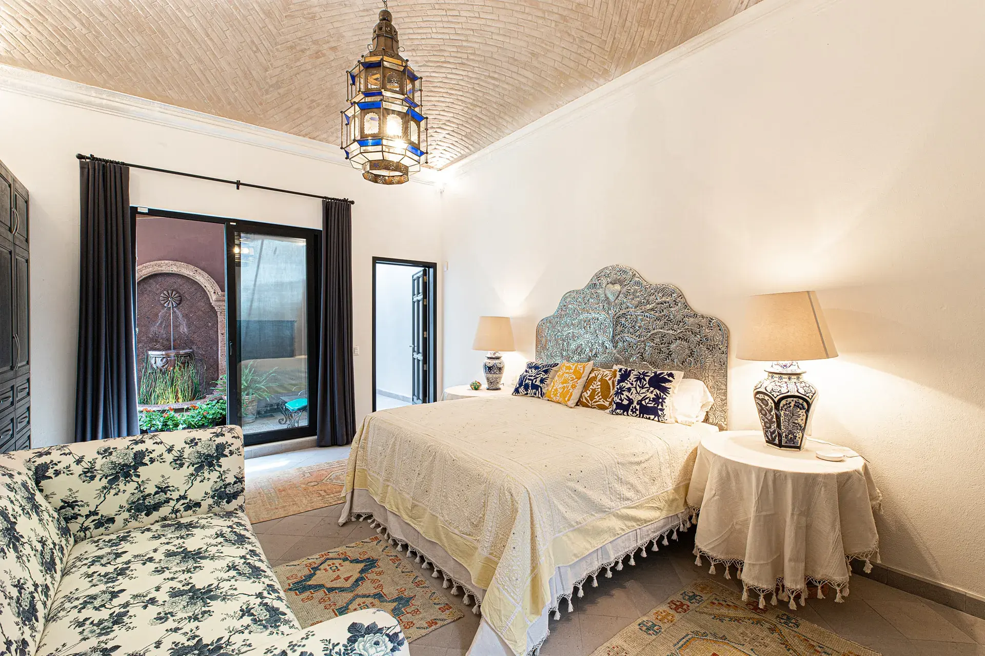 Casa Grillo, bedroom with a carved headboard, floral chair and a brick vaulted ceiling, San Miguel de Allende