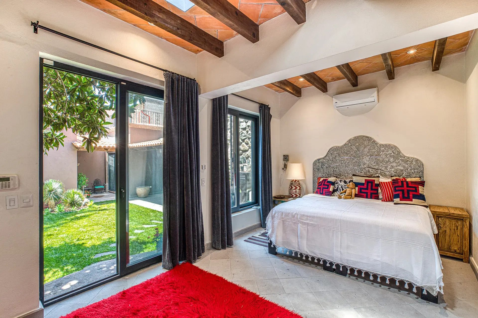 Casa Grillo, bedroom with a gray headboard, a red rug and glass doors to the garden, San Miguel de Allende