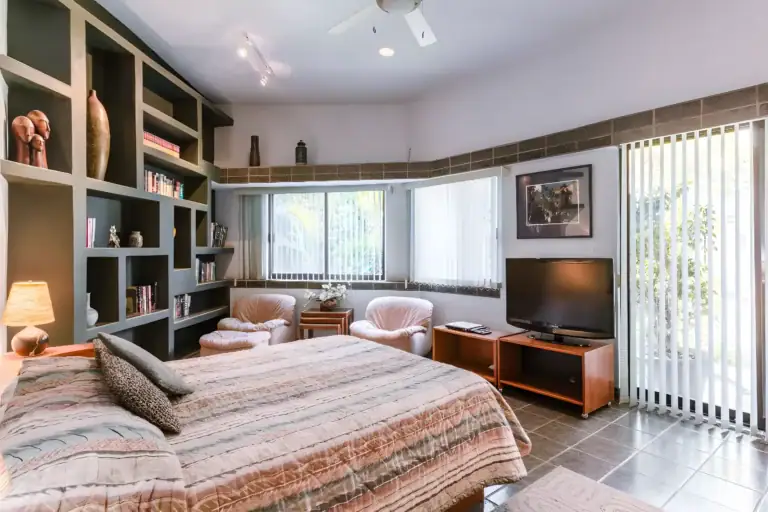 Casa Guadiana, bedroom with a striped bedspread, built-in bookshelves, a television and a garden window, San Miguel de Allende