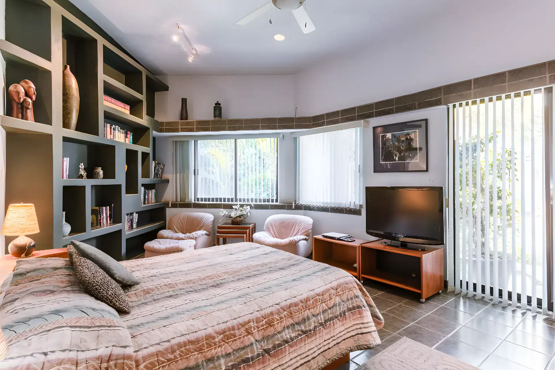 Casa Guadiana, bedroom with a striped bedspread, built-in bookshelves, a television and a garden window, San Miguel de Allende