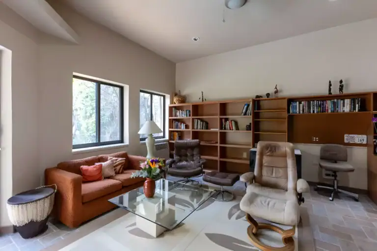 Casa Guadiana, study with a rust sofa, leather recliners, a glass table and wood bookshelves, San Miguel de Allende