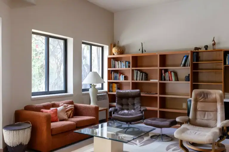 Casa Guadiana, study with wood bookshelves, recliners and a glass coffee table by garden windows, San Miguel de Allende