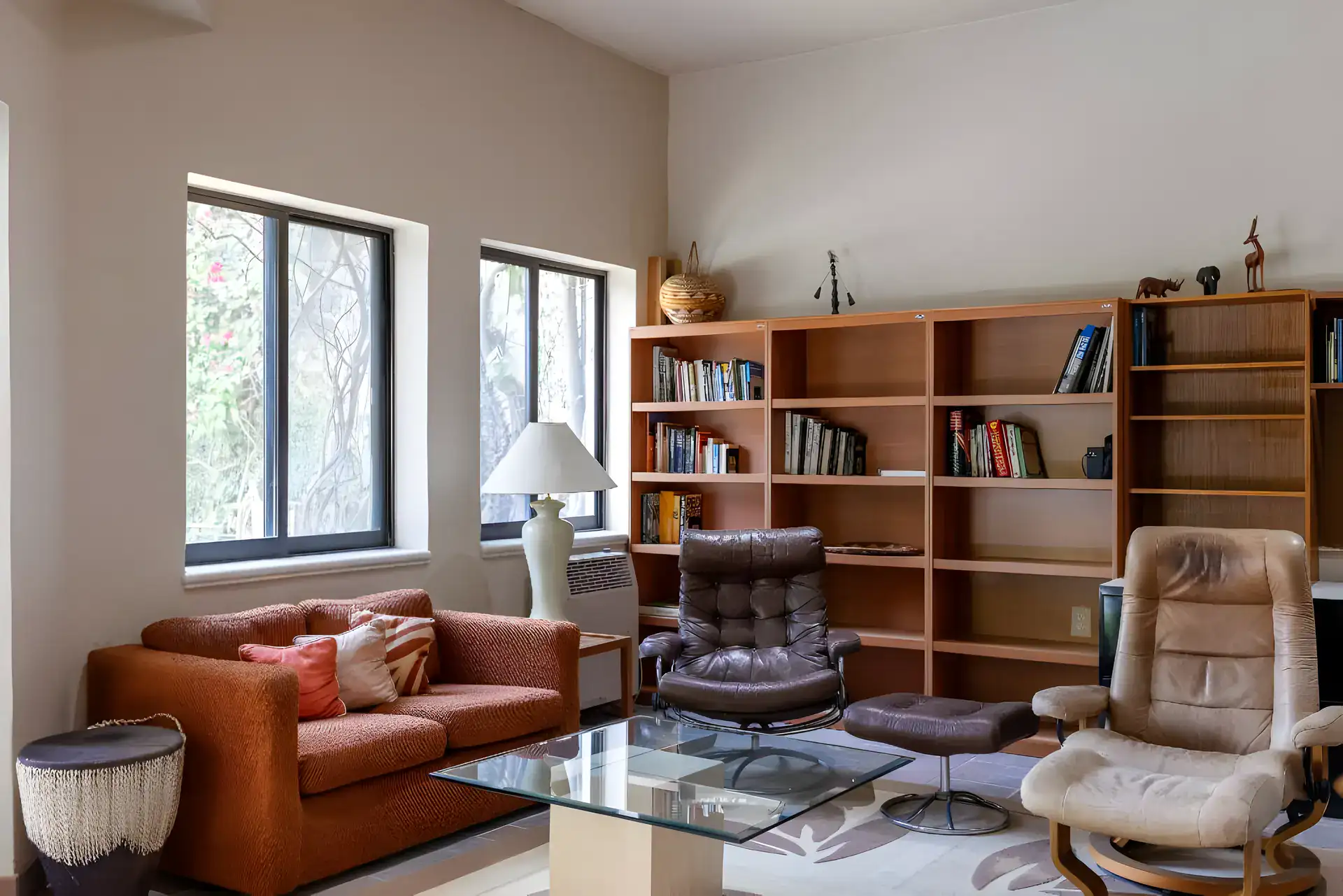 Casa Guadiana, study with wood bookshelves, recliners and a glass coffee table by garden windows, San Miguel de Allende