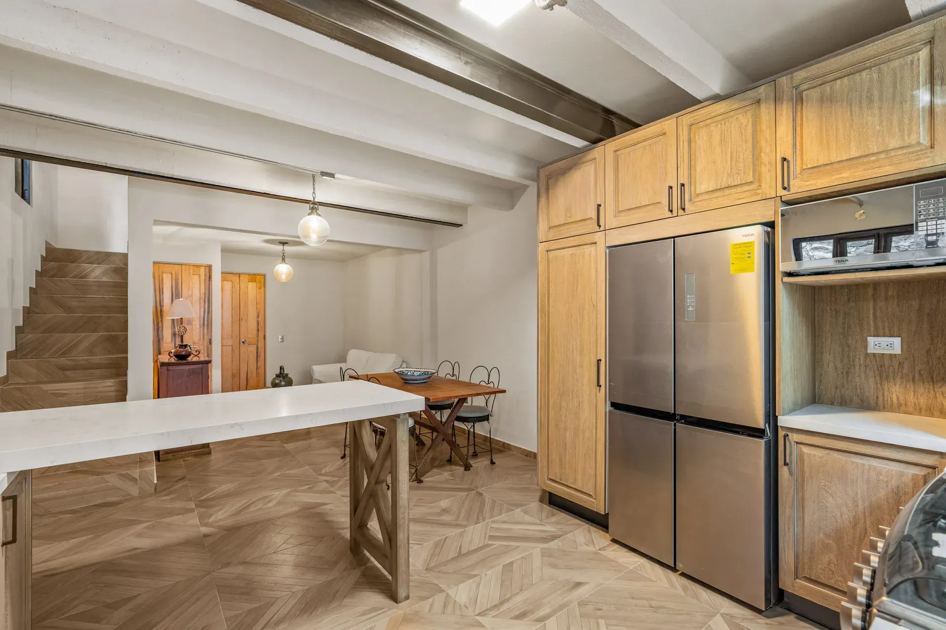 Casa Hidalgo, kitchen with natural wood cabinets, a tall stainless refrigerator, a white island counter and a herringbone floor, San Miguel de Allende