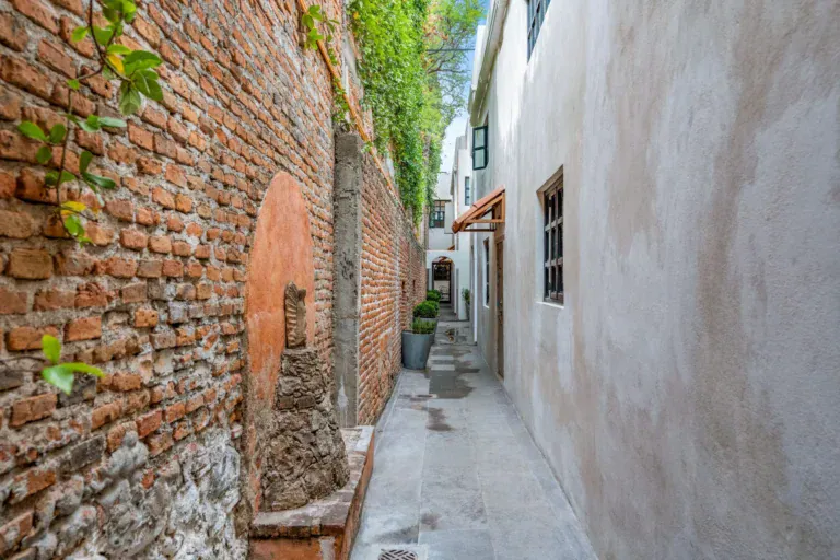 Casa Hidalgo, narrow side passage along a weathered brick wall with ivy and a pale stucco wall with a window, San Miguel de Allende