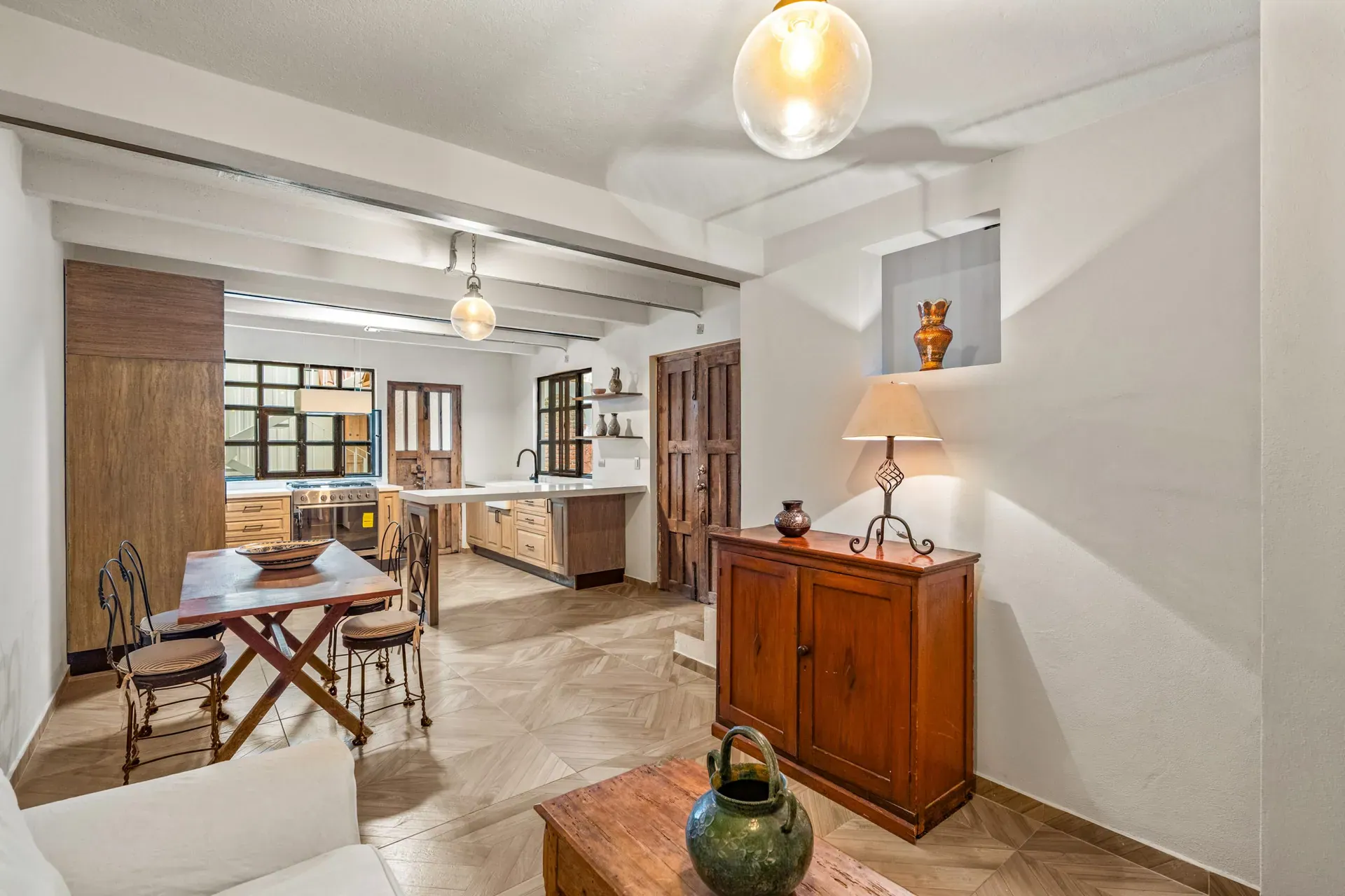 Casa Hidalgo, open living and dining area with a long wood table, black chairs, a wood cabinet and a kitchen beyond, San Miguel de Allende