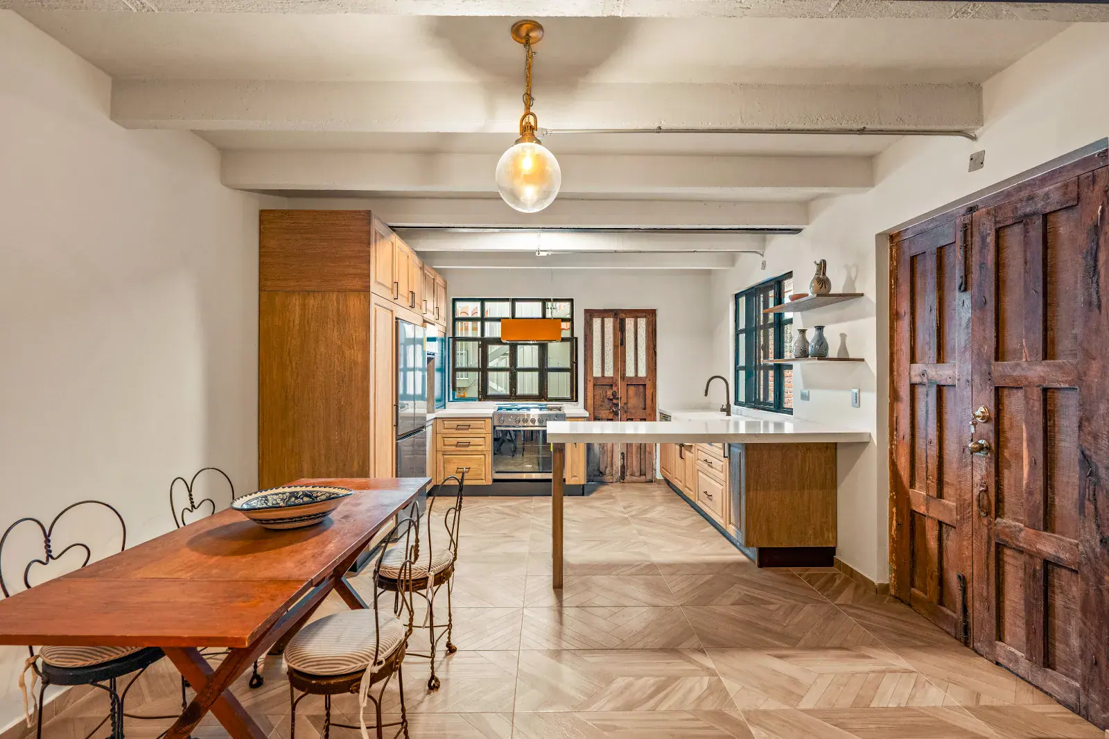 Casa Hidalgo, dining table with iron chairs, a kitchen and a carved wooden double door under exposed beams, San Miguel de Allende