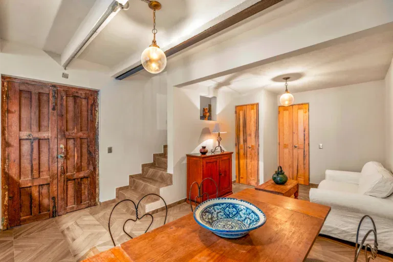 Casa Hidalgo, living area with a white sofa, a wood dining table with a blue bowl, a staircase and a carved wooden double door, San Miguel de Allende