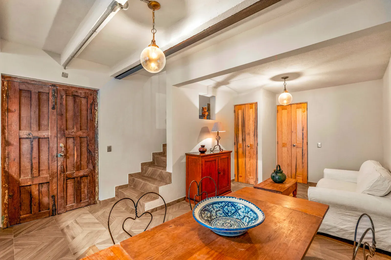 Casa Hidalgo, living area with a white sofa, a wood dining table with a blue bowl, a staircase and a carved wooden double door, San Miguel de Allende