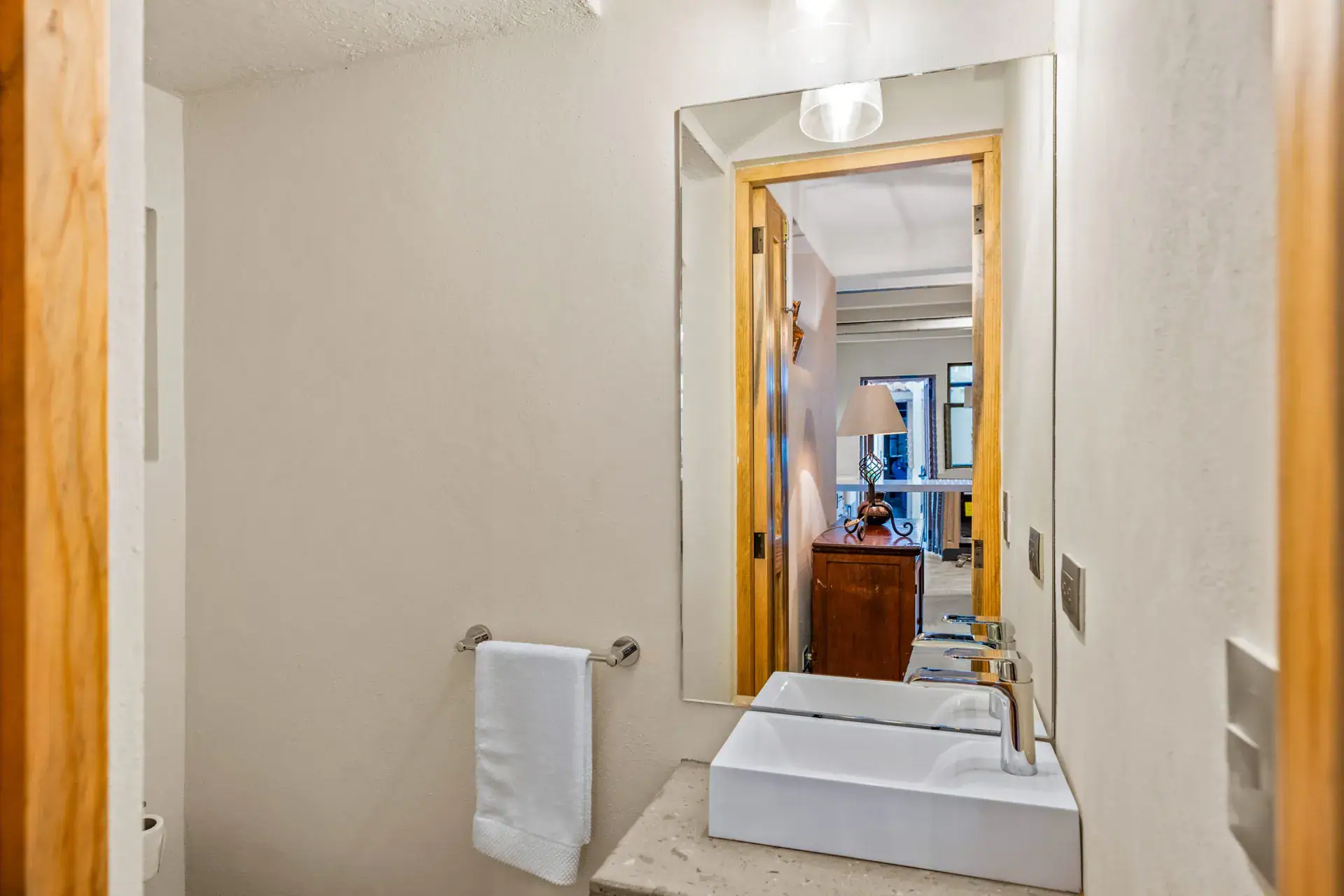 Casa Hidalgo, bathroom with a white vessel sink, a mirror showing the bedroom behind and a wood door frame, San Miguel de Allende