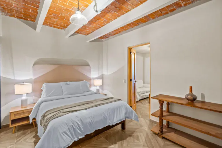 Casa Hidalgo, bedroom with a white bed, a pink arched headboard niche, rattan nightstands and a brick vaulted ceiling, San Miguel de Allende