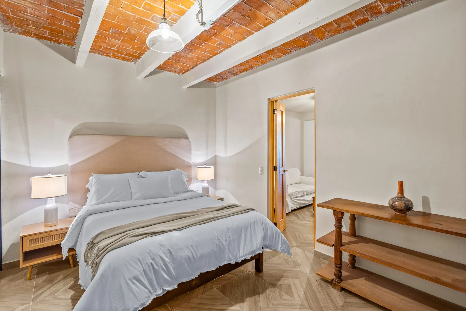 Casa Hidalgo, bedroom with a white bed, a pink arched headboard niche, rattan nightstands and a brick vaulted ceiling, San Miguel de Allende