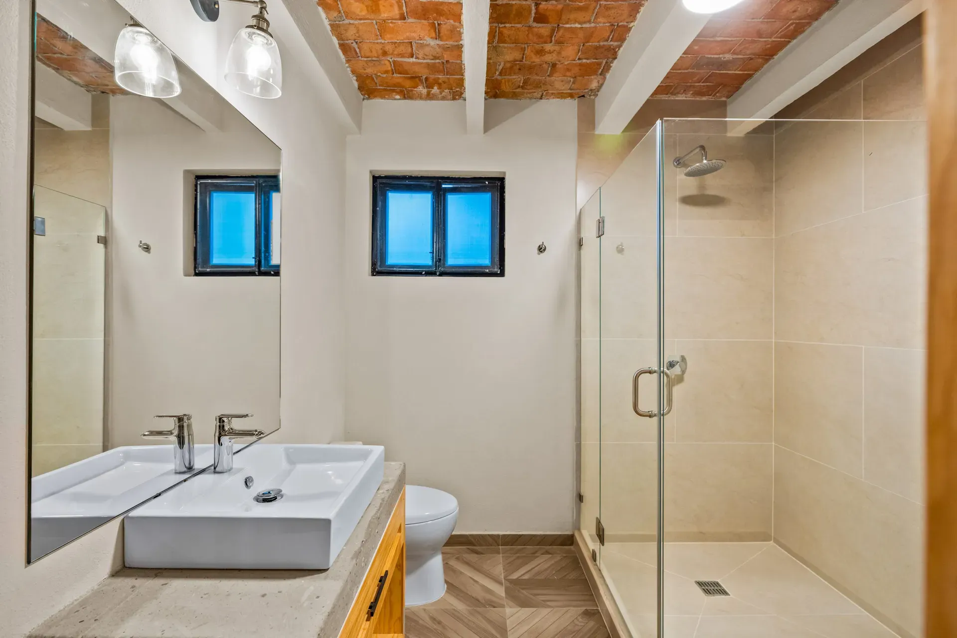 Casa Hidalgo, bathroom with a glass shower, a white double vessel sink, black-framed windows and a brick vaulted ceiling, San Miguel de Allende