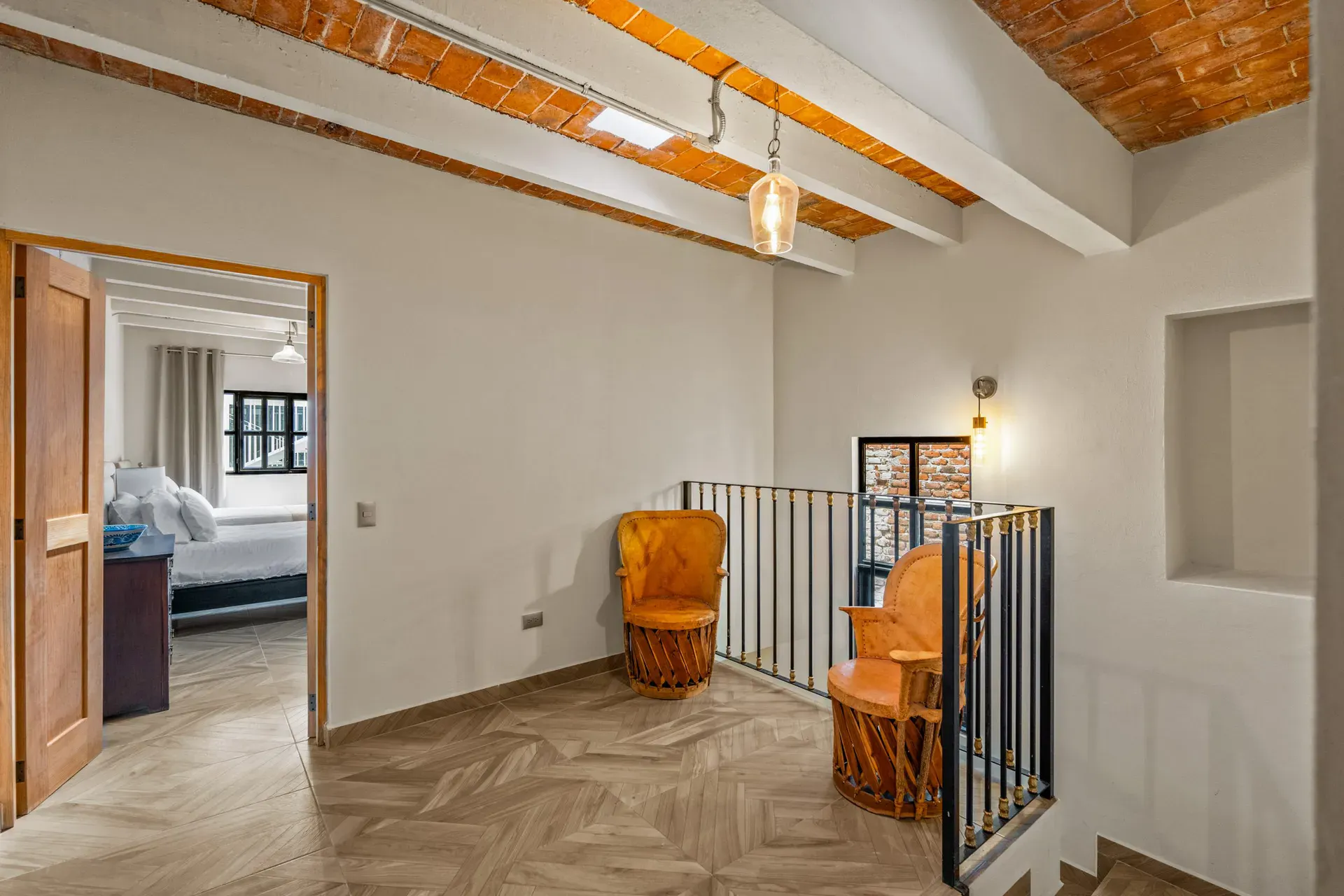 Casa Hidalgo, upstairs landing with a black railing, two equipale chairs and a view into a bedroom, under a brick vaulted ceiling, San Miguel de Allende