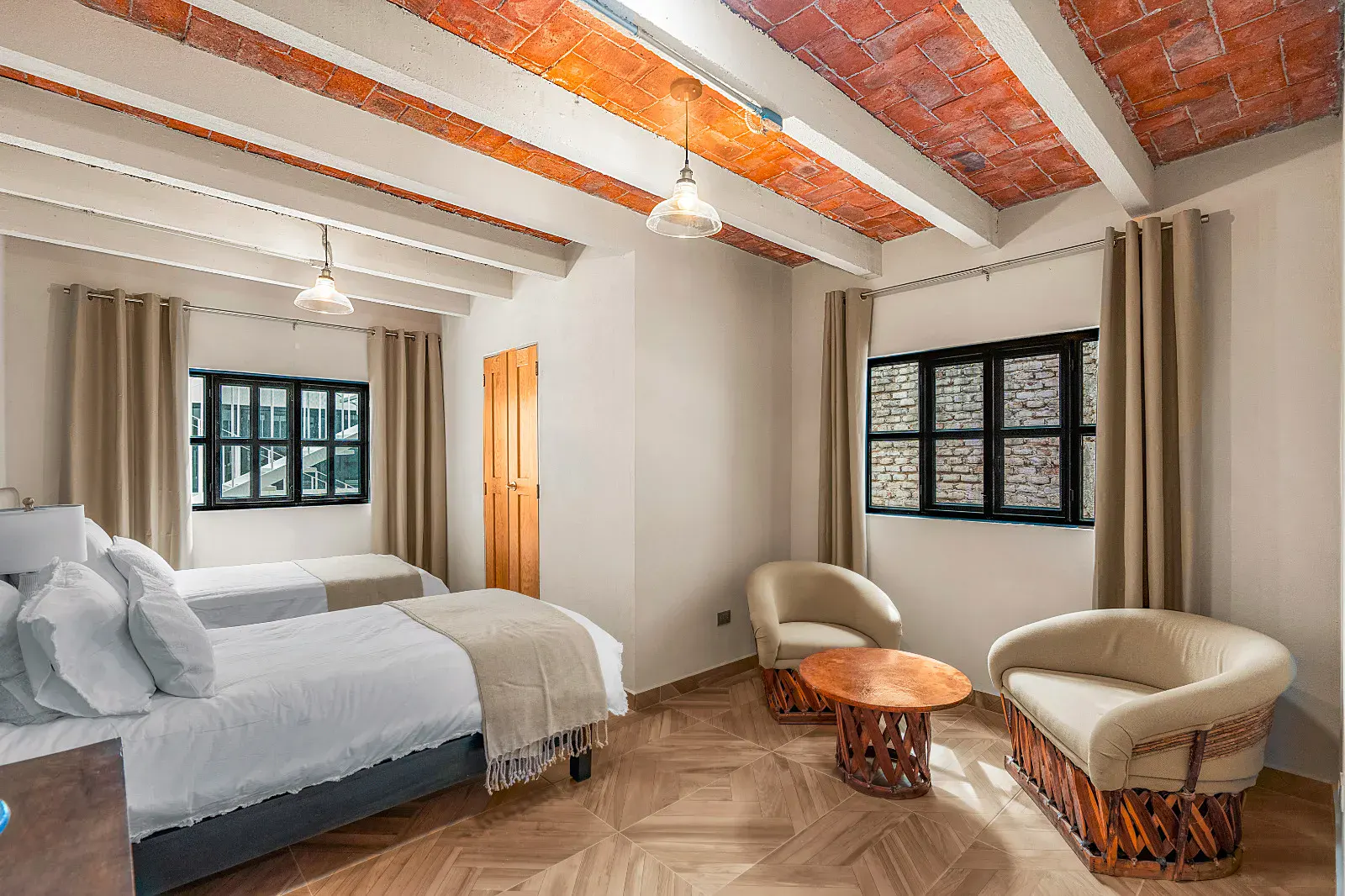 Casa Hidalgo, bedroom with two twin beds, two round leather armchairs and a wood coffee table under a brick vaulted ceiling, San Miguel de Allende