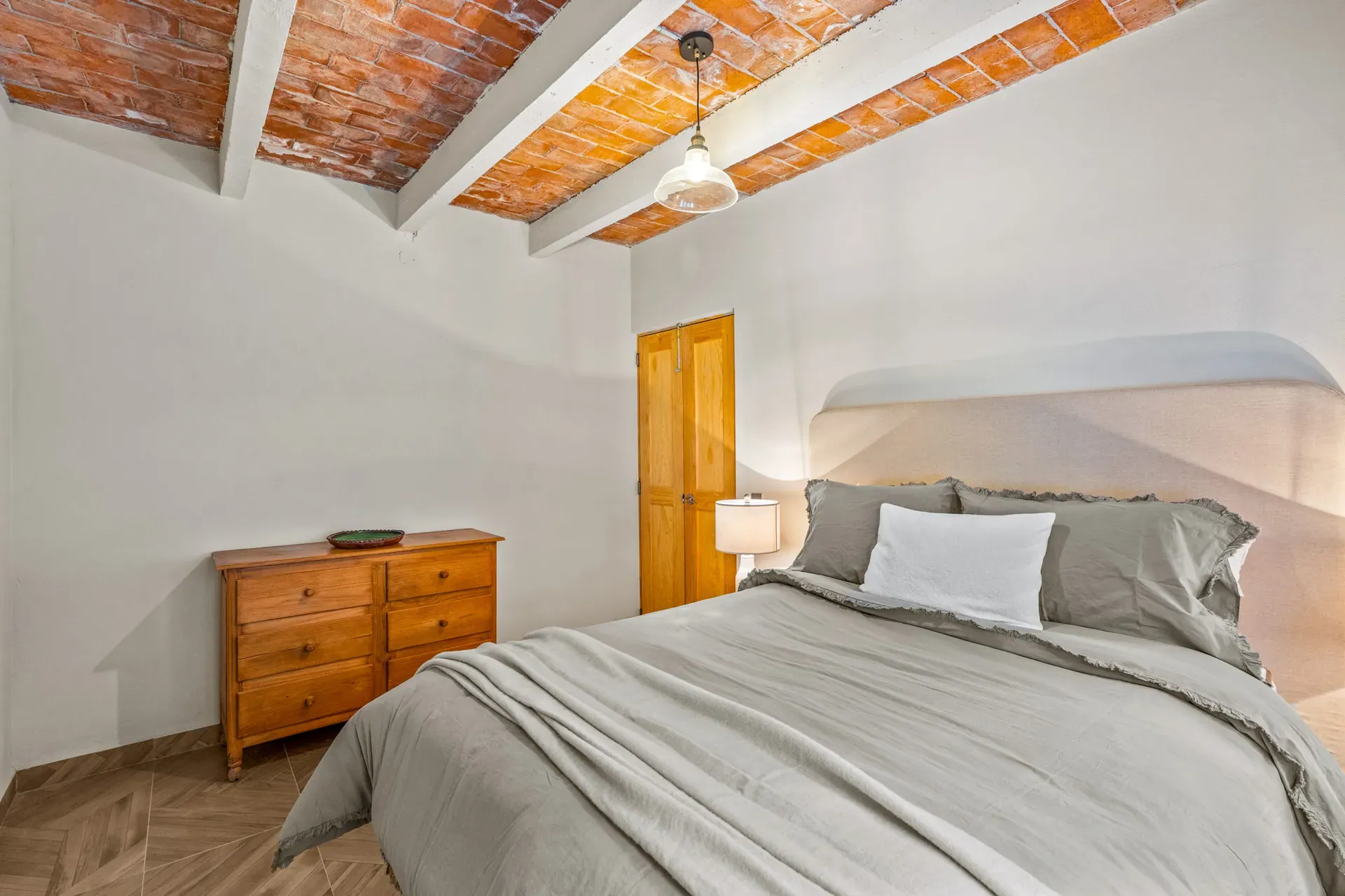 Casa Hidalgo, bedroom with a gray bed, a wood dresser and a brick vaulted ceiling with a pendant light, San Miguel de Allende