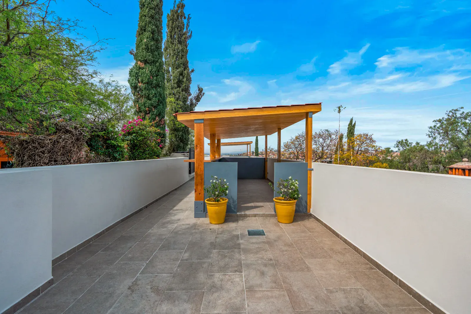 Casa Hidalgo, rooftop terrace with a tile floor, a wood and steel covered pavilion with yellow flower pots and views of trees, San Miguel de Allende