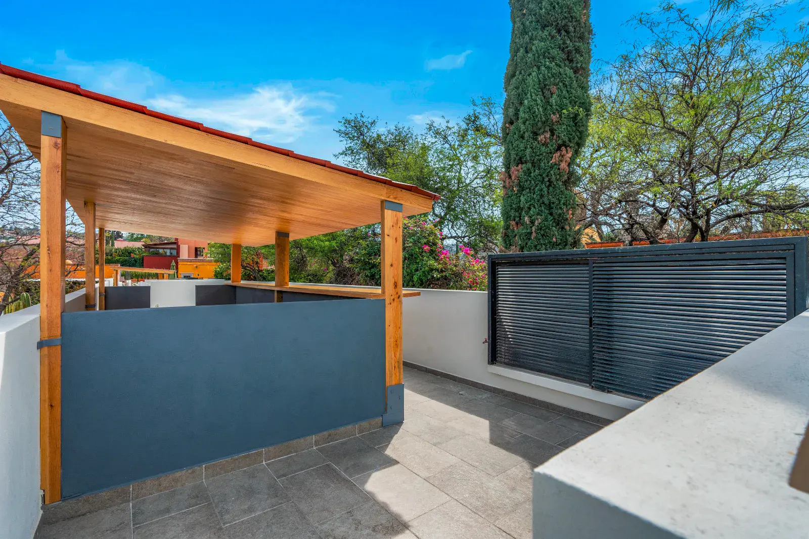 Casa Hidalgo, rooftop terrace with a covered wood pavilion, a gray wall and cypress trees, San Miguel de Allende