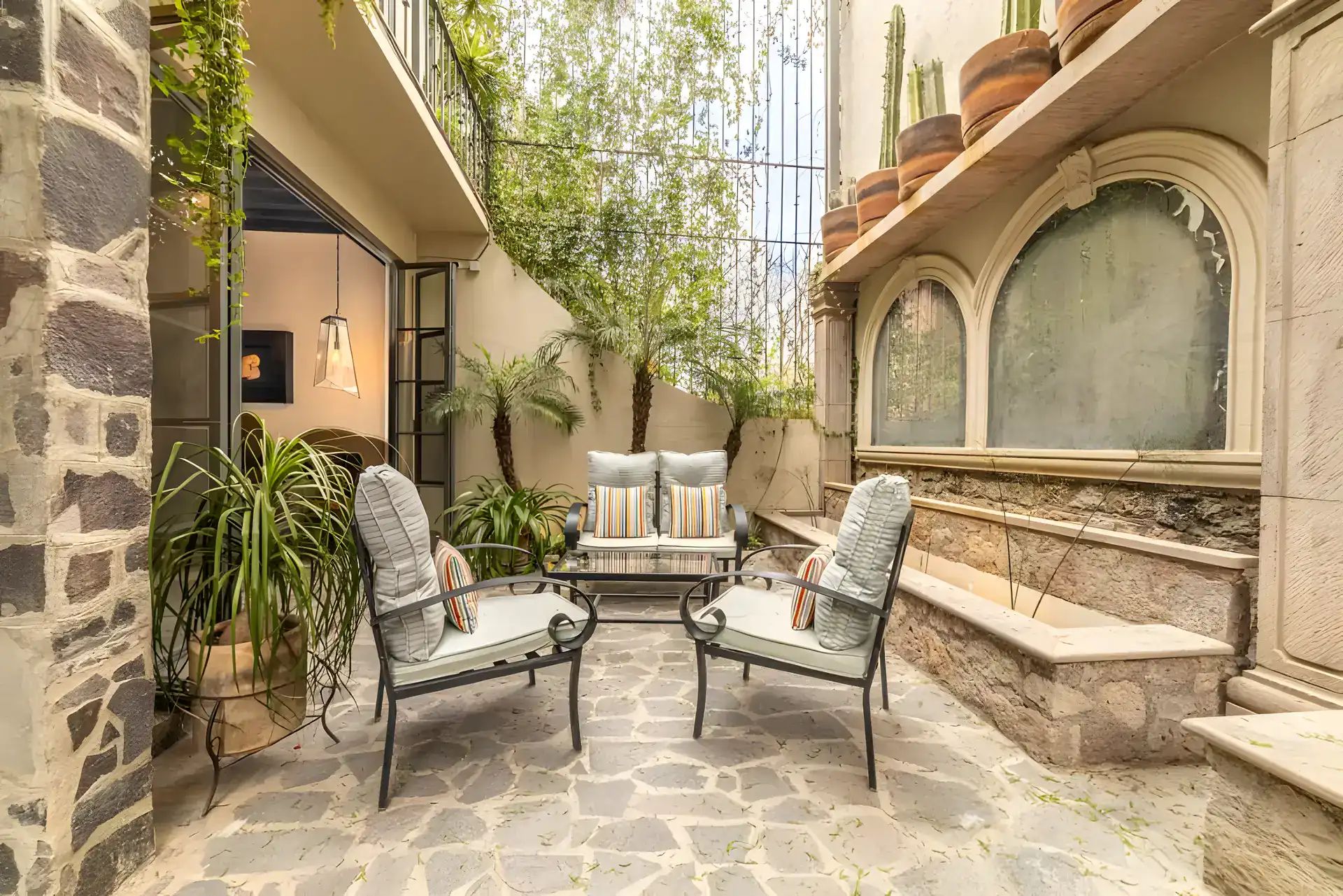 Casa Huerta, flagstone courtyard with metal outdoor chairs, a sofa, palms and a stone wall with arched niches, San Miguel de Allende
