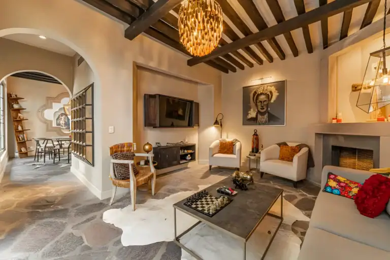 Casa Huerta, living room with a wall-mounted television, a fireplace, a checkerboard coffee table and an arched doorway to the dining area, San Miguel de Allende