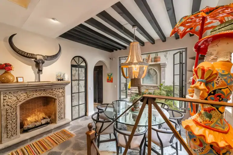Casa Huerta, dining table by a stone fireplace with a horned skull, a colorful sculpture and glass doors to the courtyard, San Miguel de Allende