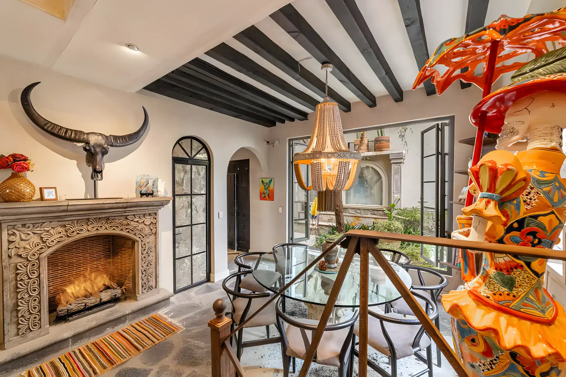 Casa Huerta, dining table by a stone fireplace with a horned skull, a colorful sculpture and glass doors to the courtyard, San Miguel de Allende