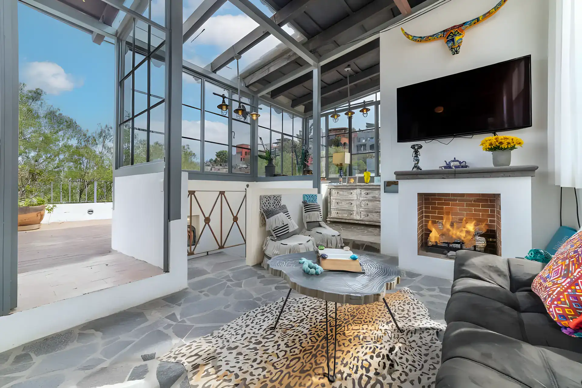 Casa Huerta, rooftop room with a television, a fireplace, a gray sofa and steel-framed glass walls and skylight, San Miguel de Allende