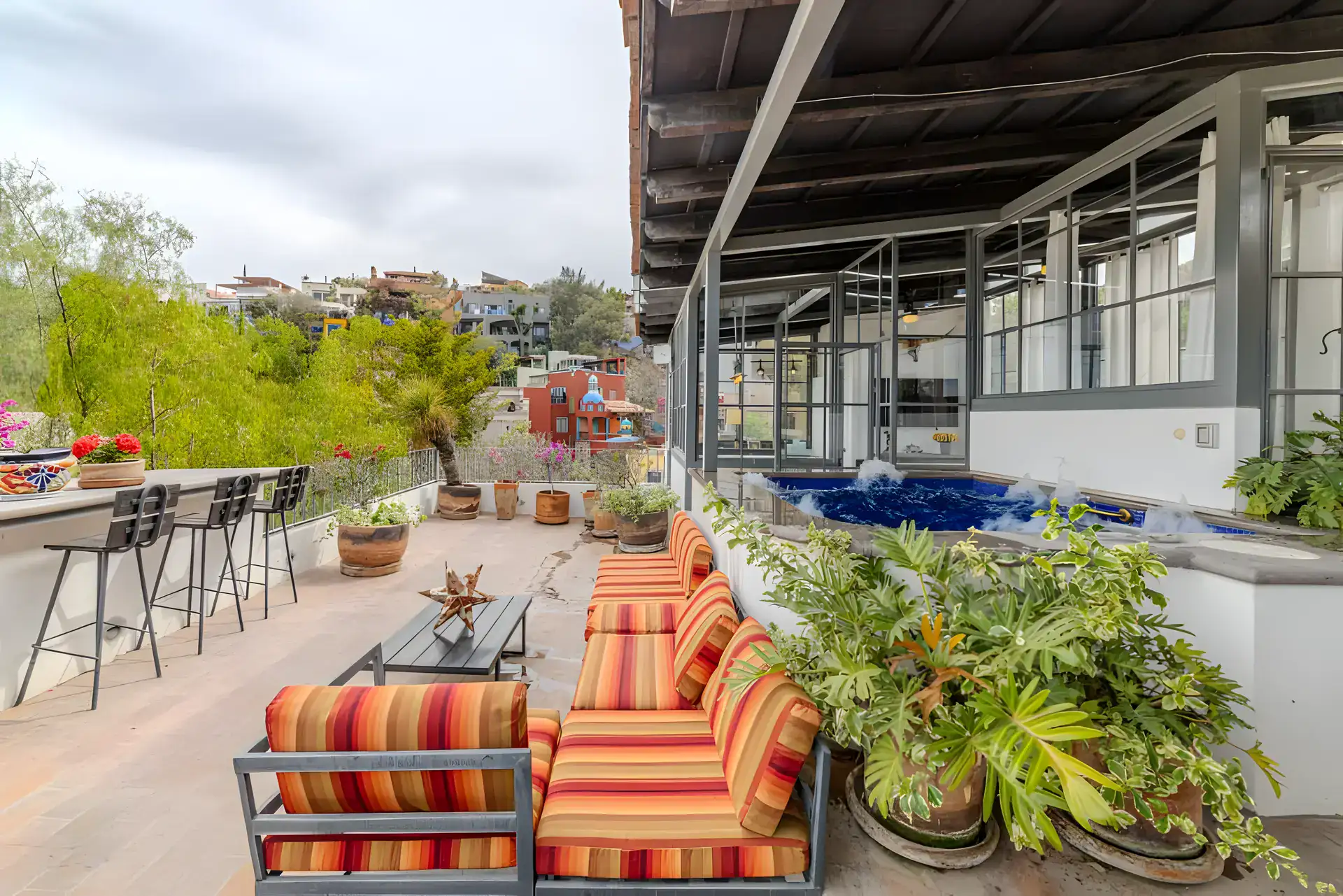 Casa Huerta, rooftop terrace with a bar counter, striped sofas, plants and a view of the town, San Miguel de Allende