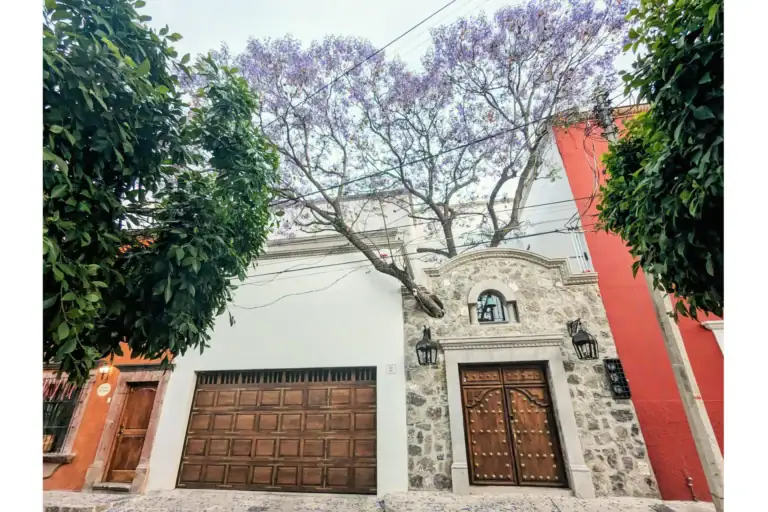 Casa Jacaranda, street facade with a jacaranda tree, carved stone portal and wood garage doors, San Miguel de Allende
