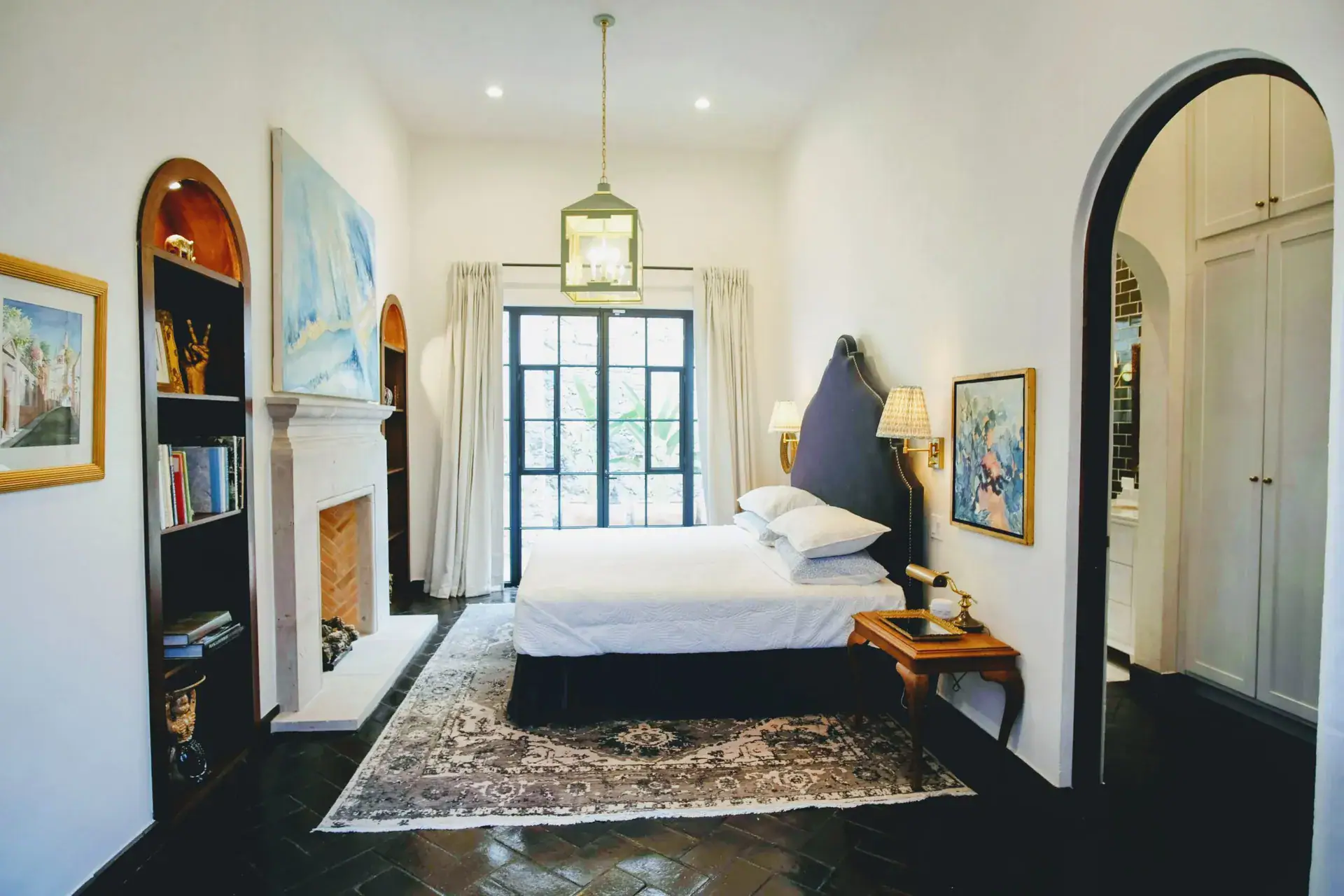 Casa Jacaranda, bedroom with a fireplace, bookshelves and a tall window, San Miguel de Allende