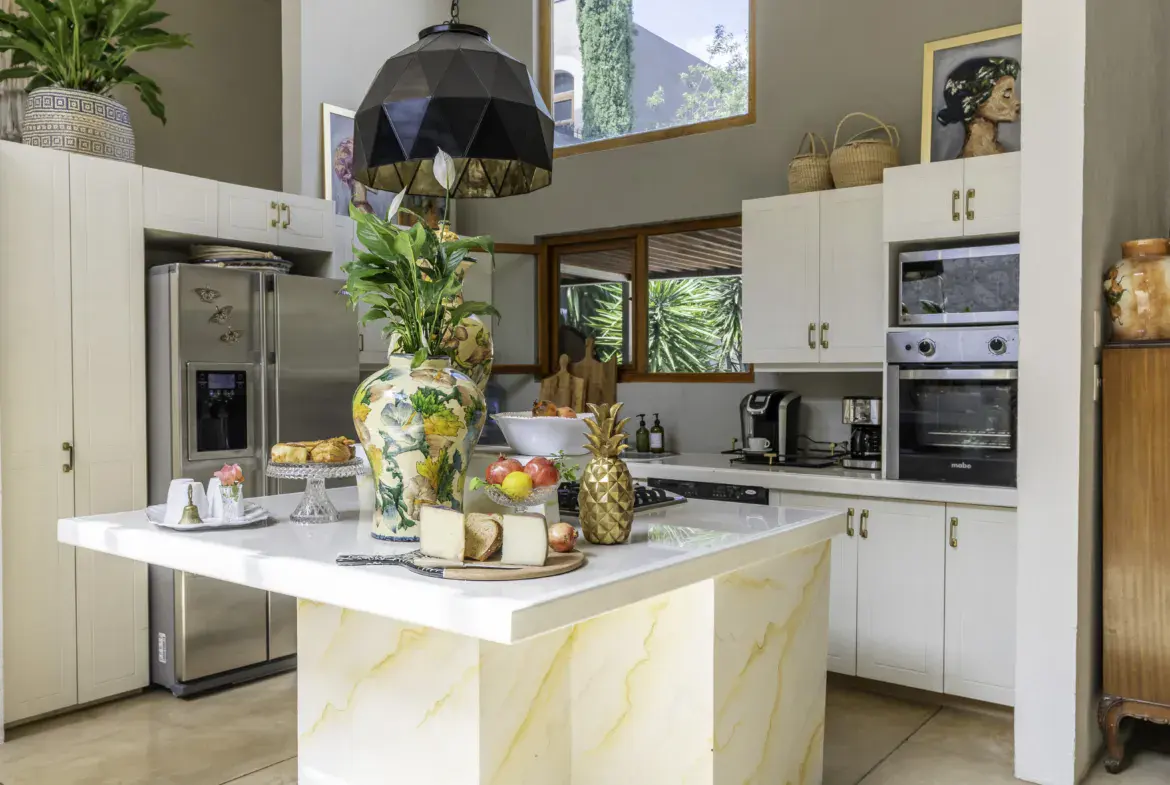 Casa Juan Guadiana, kitchen with white cabinets, a marble-look island and a black pendant, San Miguel de Allende